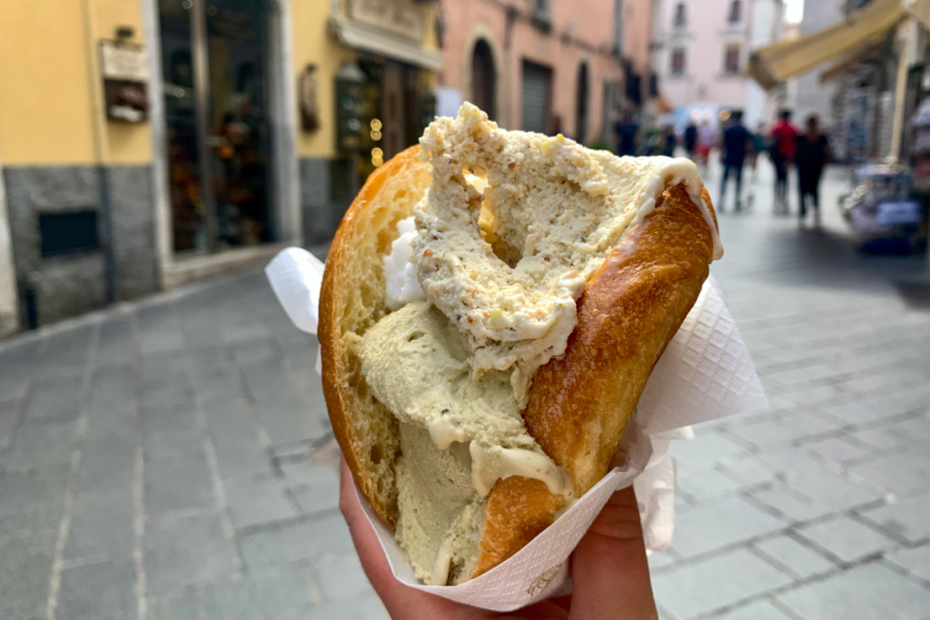 A woman's hand holding a Sicilian brioche with ice cream on a city street