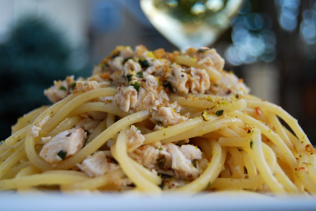 Heaping plate of spaghetti with swordfish and pistachios, with a blurry glass of wine in the background.