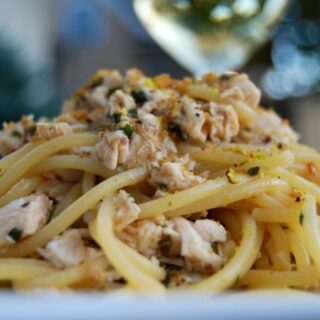 Heaping plate of spaghetti with swordfish and pistachios, with a blurry glass of wine in the background.