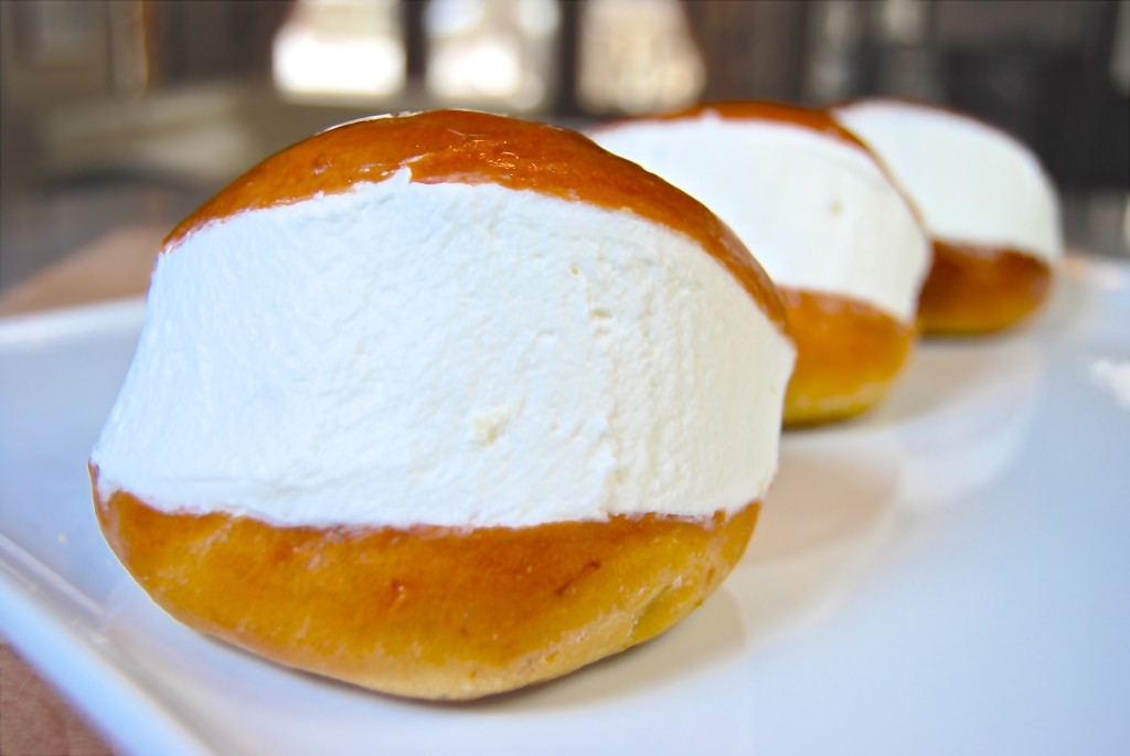 Close up picture of a maritozzo alla panna on a white plate, with other maritozzi in the background.