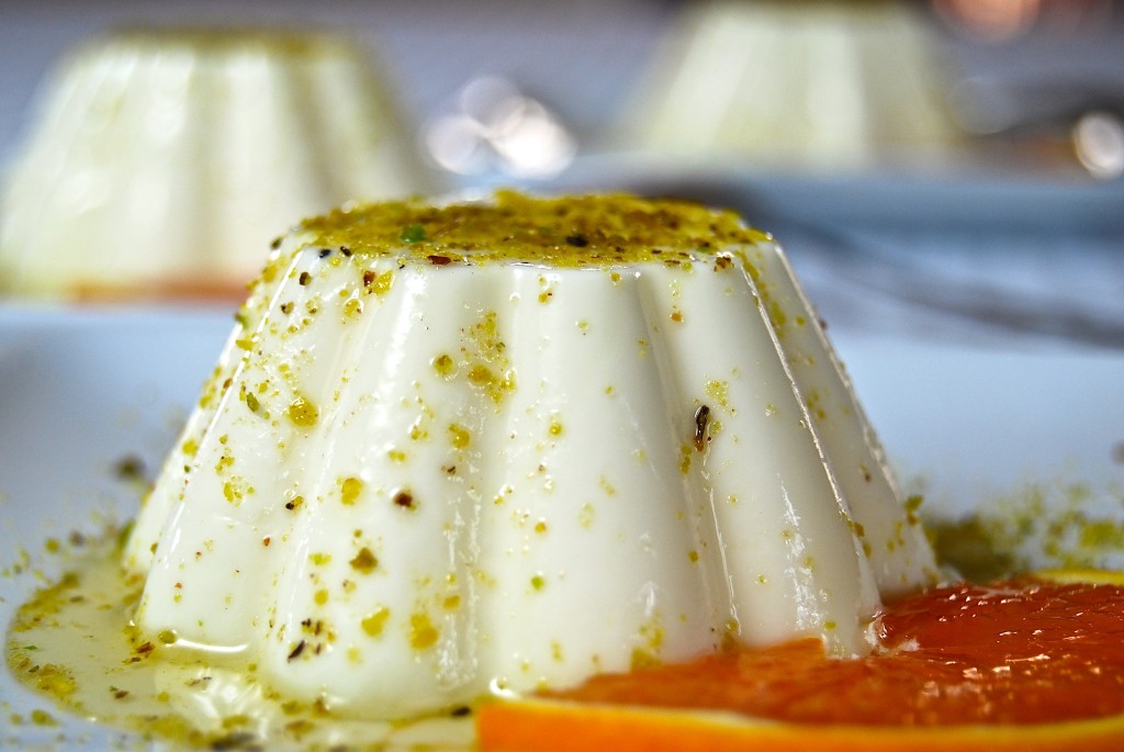 Panna Cotta drizzled in pistachio and orange sauce with an orange slice as garnish.