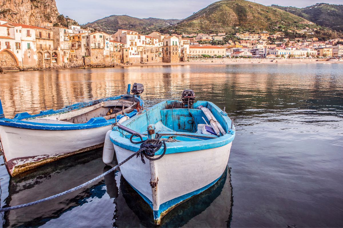 Two white and blue fishing boats with the village of Cefalù, Sicily in the background.
