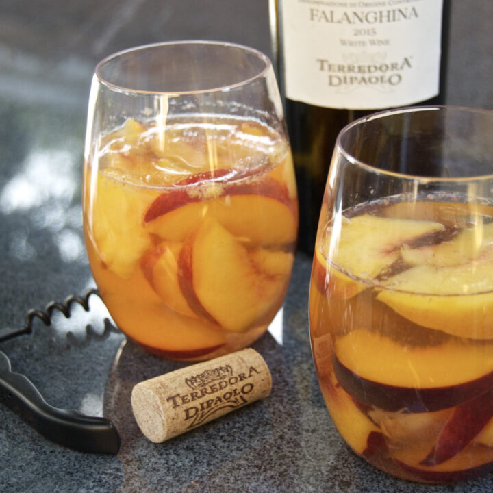 Two glasses of peaches in white wine, a corkscrew, a cork and a bottle of Terredora Di Paolo wine in the background.