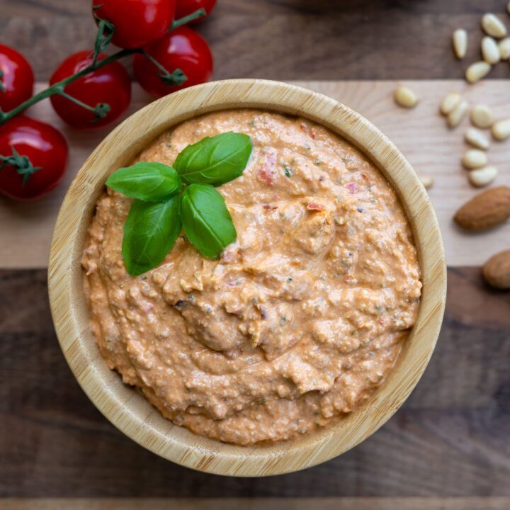 Bowl of pesto alla siciliana with some almonds, pine nuts and tomatoes in the background