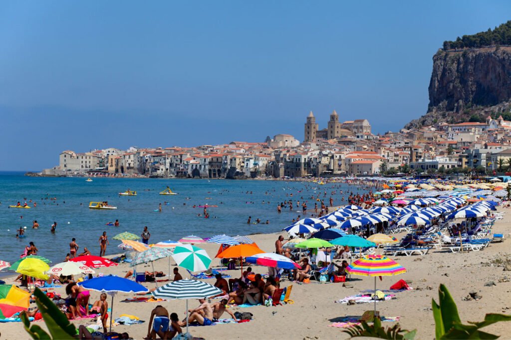 People under colorful umbrellas and swimming in the sea just outside of the town of Cefalù, Sicily.