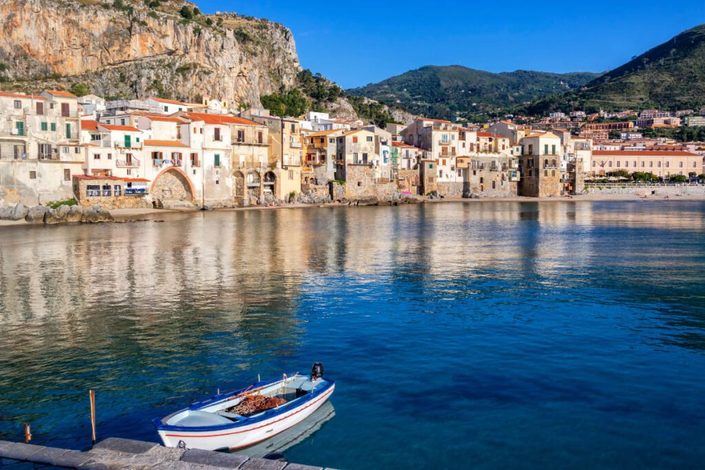 A view of the town of Cefalù, Sicily, across the water. A blue and white fishing boat is in the foreground.
