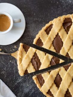 Crostata di nutella with one slice cut out, resting on a pie slicer, and white napkin and a cup of espresso.