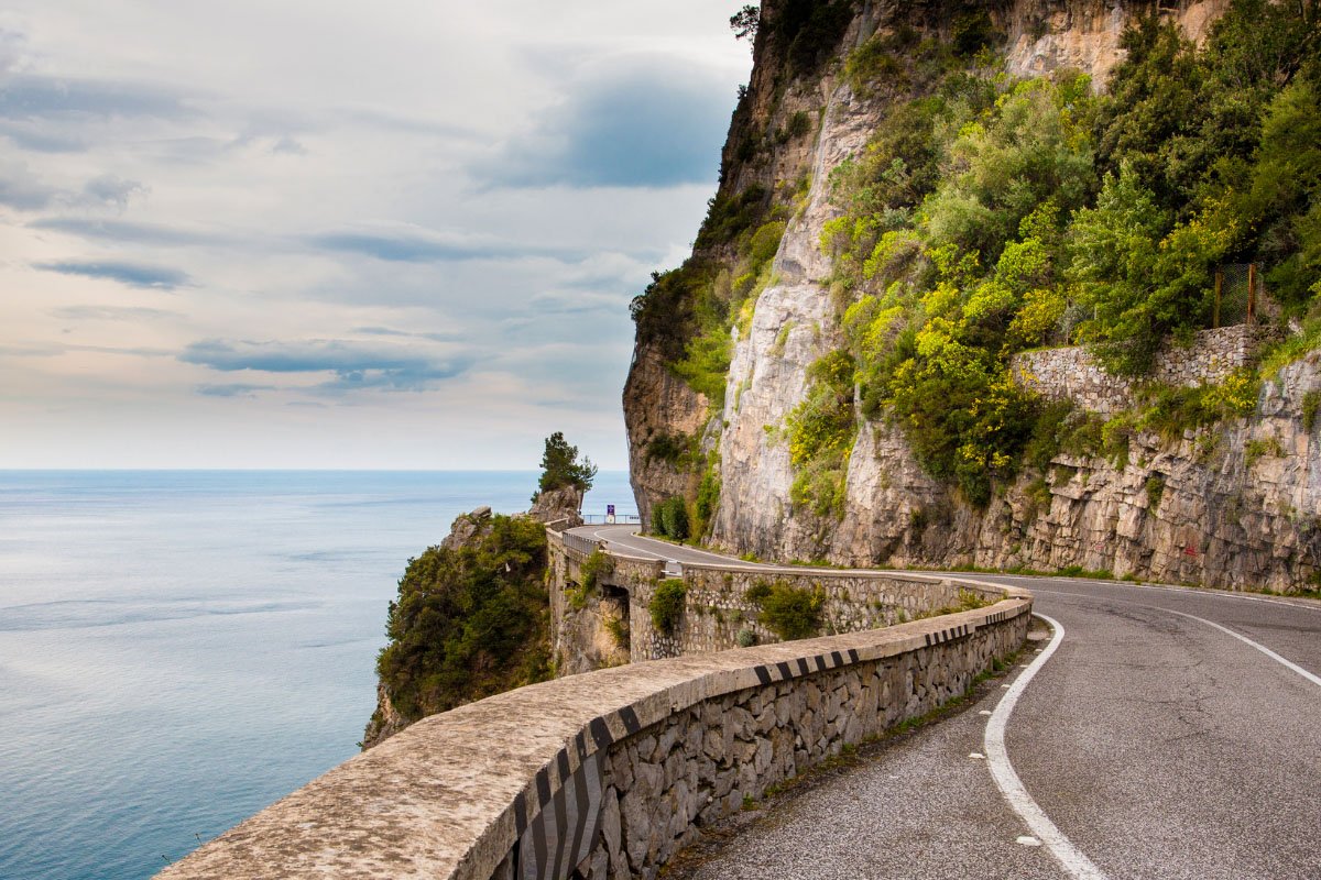 A winding stretch of Amalfi Drive, with mountains on the right and the sea on the left.