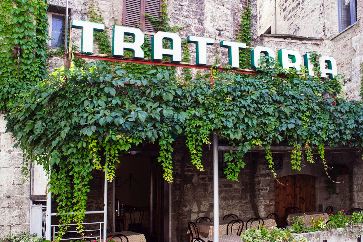 A Trattoria on a historic brick building with vines growing over the pergola