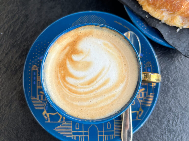 A cappuccino viewed from above, with a cornetto on a plate in the upper right corner.
